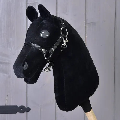 The Build your horse hobby horse from related_to_12441055625556 features a striking black head with turquoise eyes, complete with a bridle and reins, mounted on a wooden stick and set against a gray wooden panel background.