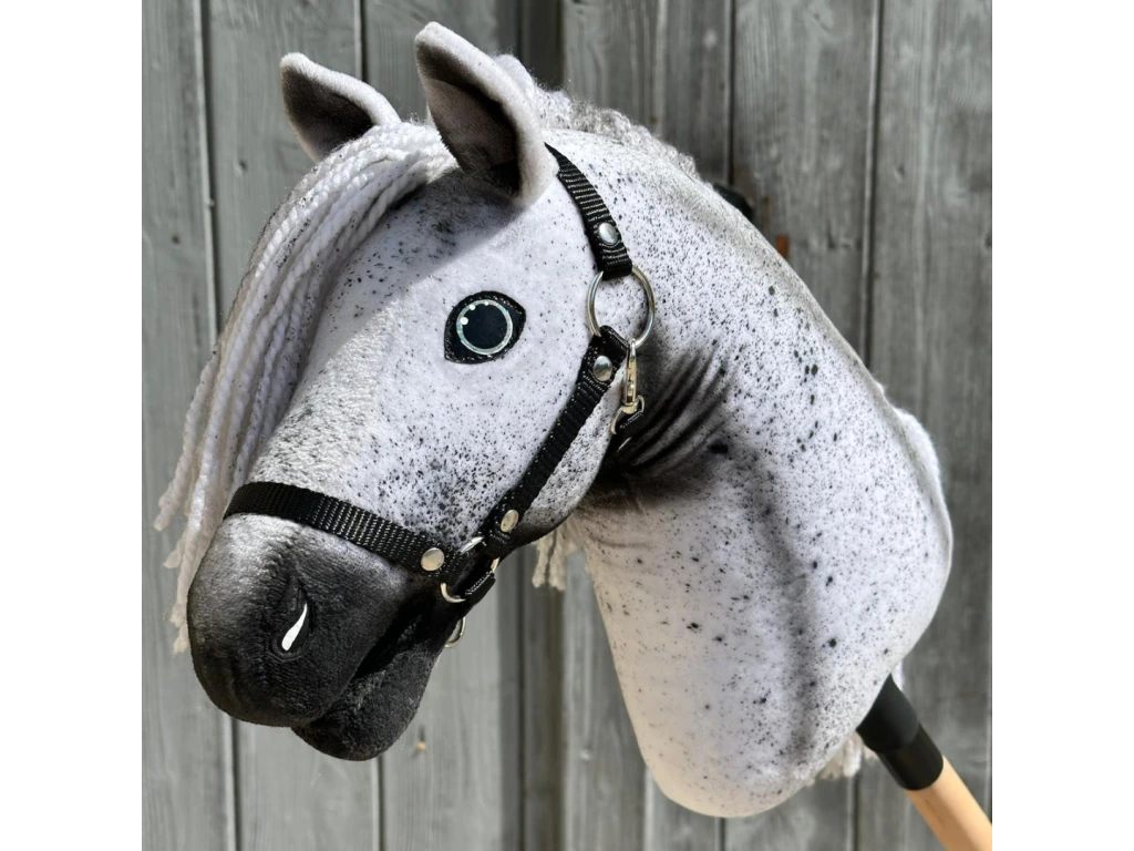 A close-up of the Hobby Horse LarDen "Naivy with Black Halter," a gray and white spotted hobby horse inspired by an Appaloosa, featuring a braided white yarn mane and black halter, against a weathered wooden background.