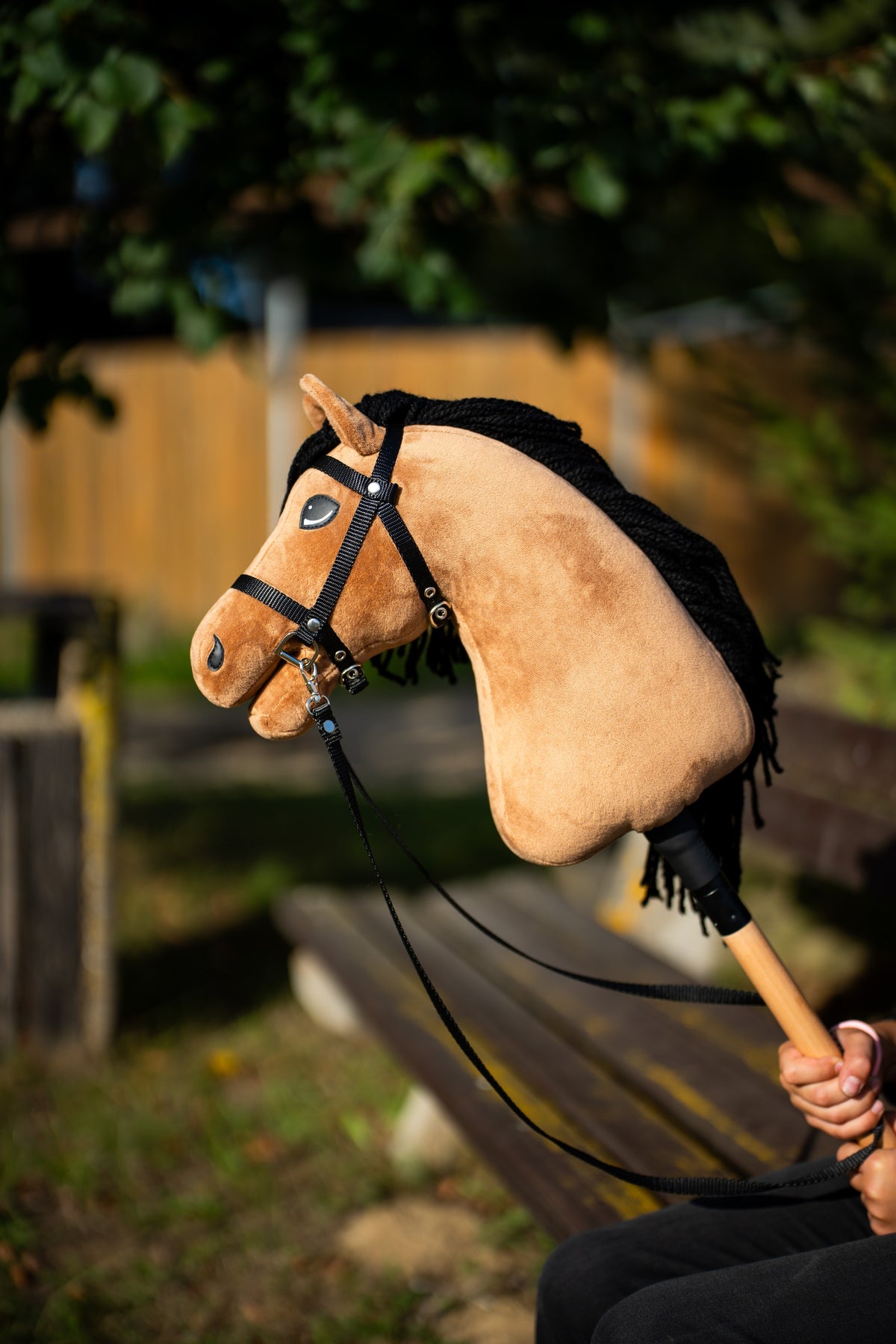 Detail photo: the head and neck of the Hobby Horse Samantha with Black Halter by Hobby Horse LarDen held up in warm evening light - sandy plush, black yarn mane - shown here with the black bridle with strap reins.