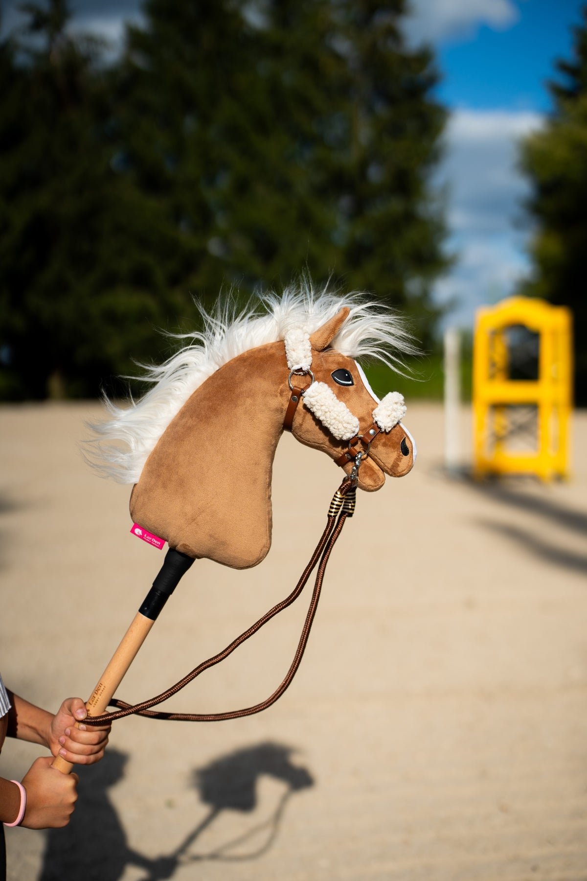 Detail photo: the head and windblown mane of the Hobby Horse Star with black halter by Hobby Horse LarDen held up on a sand arena - palomino plush, white yarn mane, white fur noseband - shown here with the brown halter with complete fur and the Vivaldi reins.