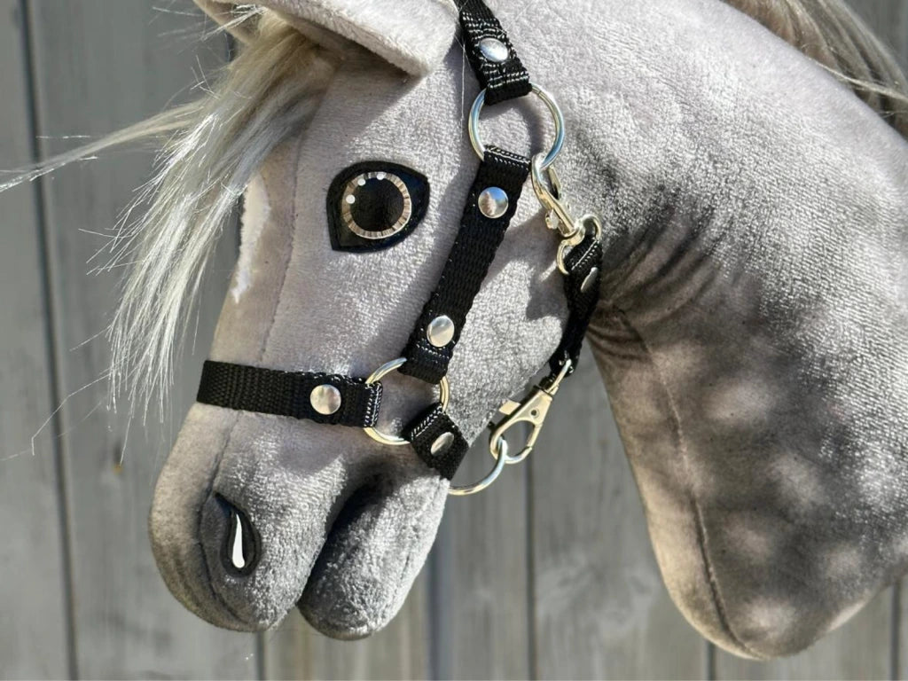 A close-up of the Hobby Horse LarDen Untamed Sweety shows the gray mare’s head with a black halter and a realistic glass eye, set against a wooden background.